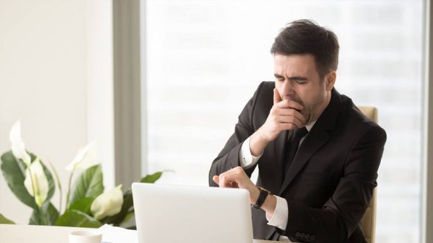 A mature business man yawning while on his laptop at work, having low energy