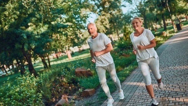 A mature couple running outside and exercising with a green scenery