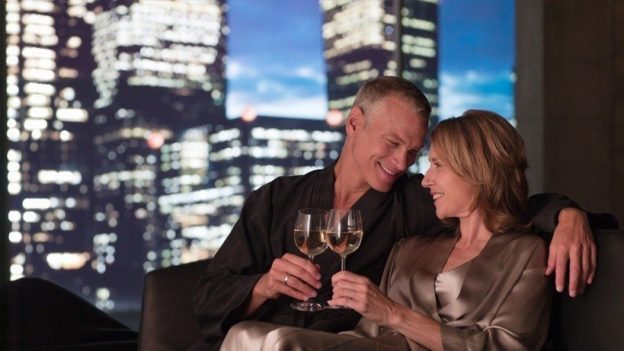 Older man and woman sitting together with white wine, with a city background