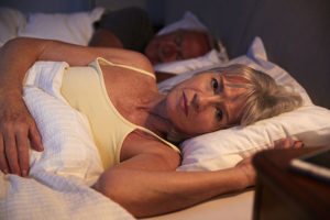 Mature woman lying in bed with her husband having trouble falling asleep experiencing the effects of anxiety 
