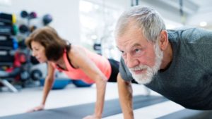 Older man and woman doing exercise at the gym to practice healthy living