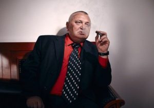 Overweight mature male in suit smoking a cigar in empty room which can cause erectile dysfunction