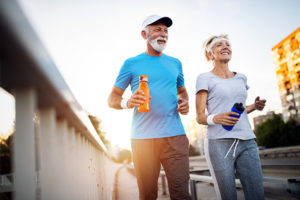 Mature couple jogging and running outdoors in the city, Mature couple carrying reusable water bottles while jogging through the city, exercising to lower high cholesterol  