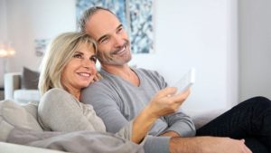 An older man and woman sitting and smiling while watching television