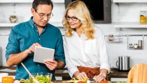 A mature man and woman preparing a healthy meal and looking at a recipe together for healthy living