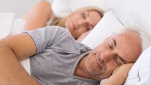 Couple peacefully sleeping in a bed with all white sheets/blankets getting enough sleep for optimal health