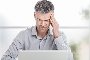 Mature male struggling with migraine while staring at laptop experiencing symptoms of high blood pressure