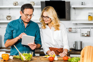mature couple reviewing recipe on tablet while cooking in kitchen, cooking food to reduce anxiety 