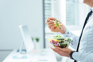 Businessman eating a pre-packaged salad while standing in office, a great diet or metabolic syndrome