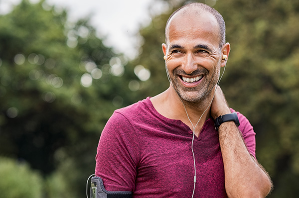 Mature man smiling as he jogs in tree-covered area, exercising and boosting testosterone naturally 