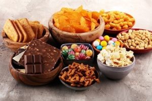 Chocolate, chips, candy, cookies, and junk food in bowls on solid background are all foods to avoid for weight loss 