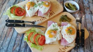 Food on 2 cutting boards, including fried eggs, tomatoes, lettuce, with a fork and knife sitting on a wooden table, a healthy plate of high protein foods that help maintain healthy habits