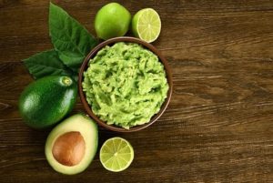 Guacamole in a bowl surrounded by avocados, a healthy fat snack choice