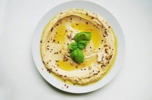 A healthy snack of seasoned hummus with oil in white bowl on white background