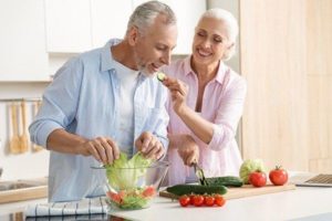 Mature woman eating man cut cucumber as they make a fresh salad in their kitchen, combating erectile dysfunction through diet