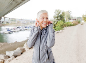 Happy mature woman listening to music with earphones while jogging, exercising for bone health to prevent osteoporosis