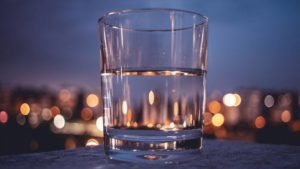 a glass of water sitting on a cement wall with blurred lights behind it