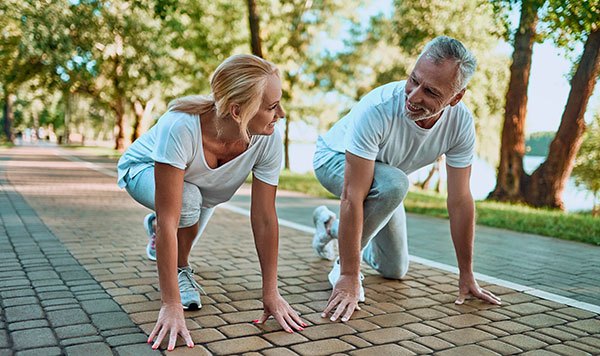 Mature couple in runners pose getting ready to race in a park at a healthy weight preventing insulin resistance