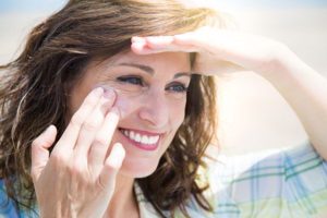 Mature woman smiling while rubbing sunscreen on face decreasing her vitamin d levels