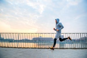 Man in grey joggers exercising along ocean side at sunrise to increase mental acuity
