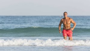 Athletic middle aged man running out of ocean maintaining a healthy weight