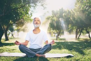Mature old man doing yoga outside in a park on a sunny day releasing stress .