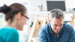 mature businessman smiling while assisting younger female coworker with strong brain health
