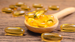 Fish oil supplements in wooden spoon on table