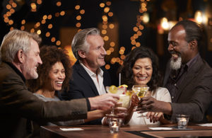 mature group of friends drinking alcohol in a bar, things to avoid doing daily while trying to eat healthy while traveling 
