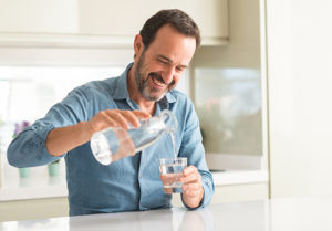 man pouring water into glass cup while sitting in clean kitchen, drinking lots of water to stay healthy while traveling
