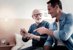 An older man and a younger man sitting on a bed smiling while looking at a photograph, making lifestyle choices that can be optimized to minimize Alzheimer’s risk