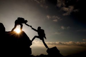 silhouetted man helping partner climb large boulders, being motivation buddies to stay on track with exercising and diet