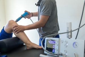 Medical technician using shockwave therapy system on patient’s knee for erectile dysfunction treatment