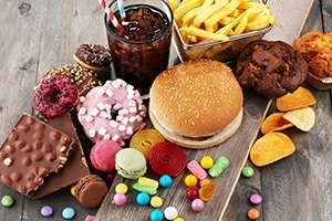 Unhealthy, processed foods including fries, soda, chips, cookies, chocolate, donuts and candy sprawled out on a wooden counter. Saturated fats that can lead to heart disease.