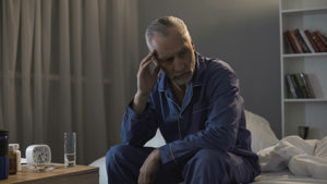 Man sitting up in bed unable to fall asleep experiencing a sleep disorder that can lead to depression 