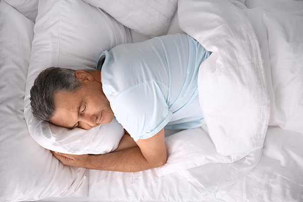 Man in blue shirt sleeping on side getting sleep for optimal testosterone levels