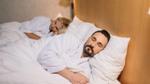 A couple, all in white, asleep in bed to get quality sleep for healthy living