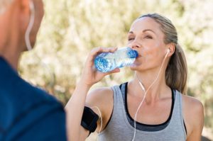 Woman drinking water and hydrating while exercising with mature male partner