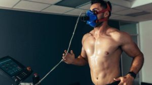 A man with a shirt off and a VO2 Max mask on while he exercises for a full body evaluation alongside testosterone therapy