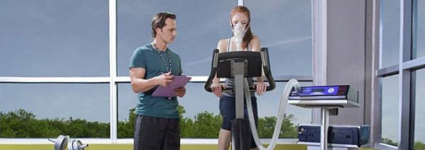 Woman taking a VO2 max test on a bike while being monitored by an exercise physiologist 