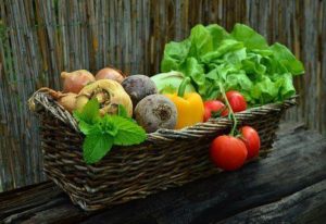 brown basket on rustic wooden table with raw vegetables: red beets, turnips, tomatoes, spinach, yellow pepper are all examples of food that can help lower cholesterol levels 