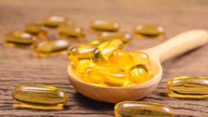 Fish oil supplements in a wooden spoon and spilled around and laying on a wooden table, factors that can lead to Alzheimer's disease