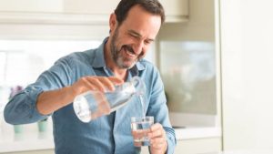 Smiling mature man with a neat beard pouring a glass of water to stay hydrated for healthy living