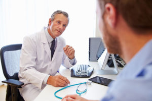 Mature doctor speaking to male patient while sitting at his desk about adrenal fatigue