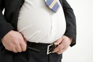 fat man trying to fasten his belt but unable to do so, the result of eating lots of processed foods