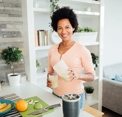 Mature woman in bright kitchen pouring protein shake from blender into cup
