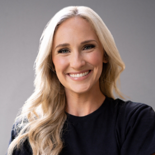 A woman with blonde hair and a black shirt smiles broadly at the camera.
