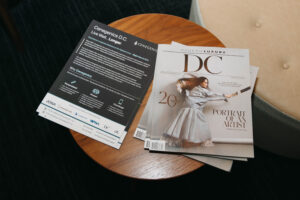 A brochure from Cenogenics D.C. and a copy of Modern Luxury DC magazine are on a wooden table next to a chair. The magazine features a woman on the cover with the title "Portrait of an Artist".